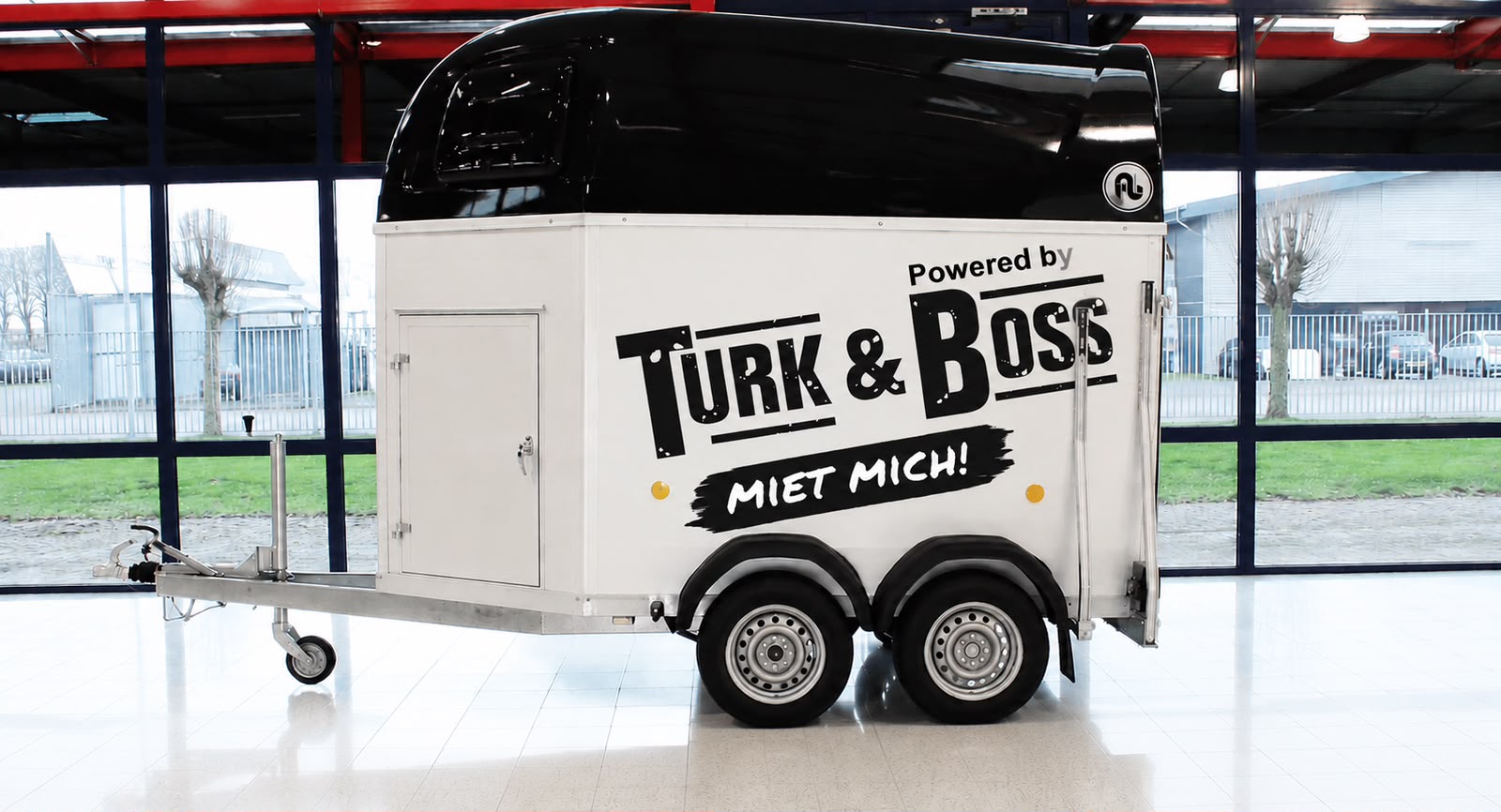 Weiß-schwarzer Pferdeanhänger mit Turk-&-Boss-Beschriftung in der Halle